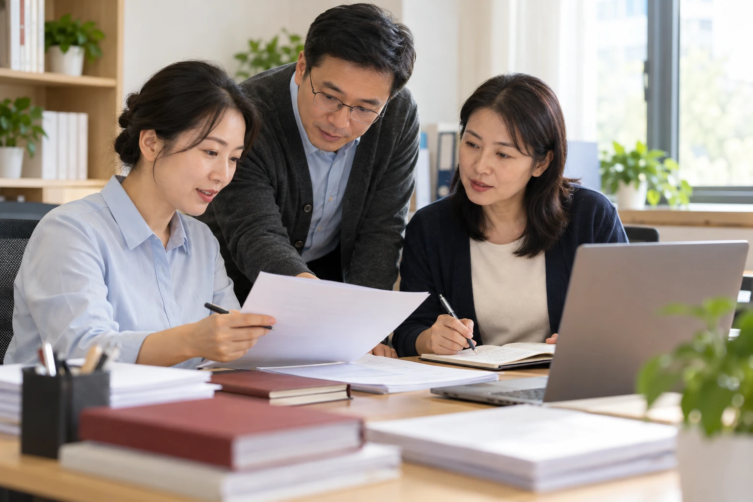 班级服务人员在明亮办公室共同阅读反馈资料并做笔记,电脑背面朝镜头,业务场景示意